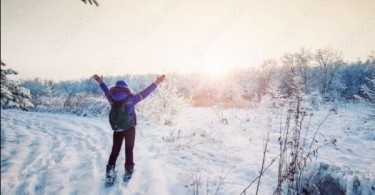 Snowshoer on trail with open arms towards sunset